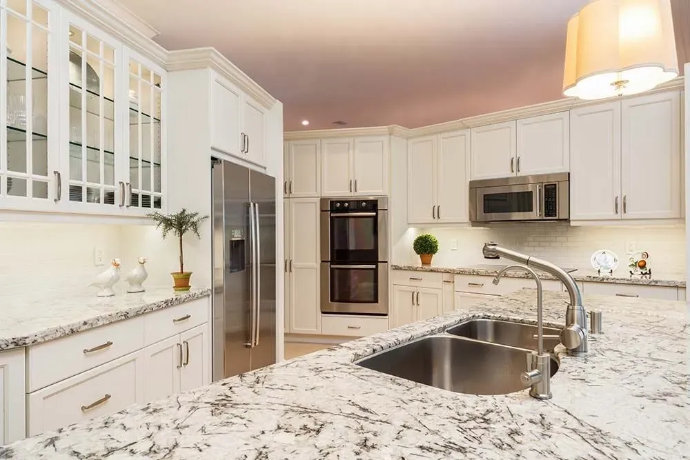 A granite peninsula with heavy black and grey veining on a white base, wrapped around a stainless double sink in a white kitchen
