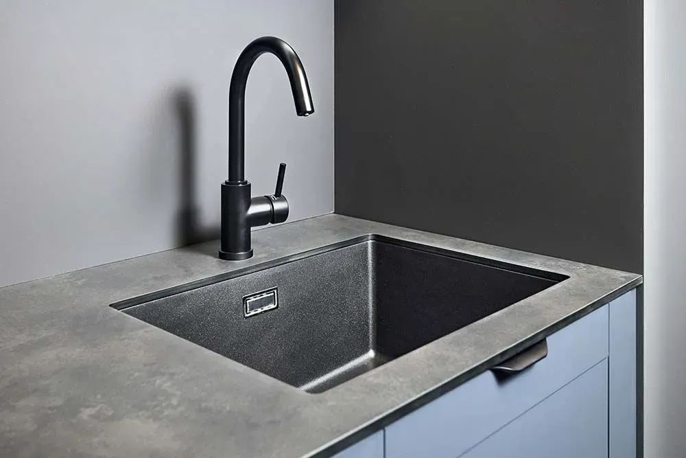 A grey stone-look countertop with a matte finish beside a dark undermount sink and a black faucet