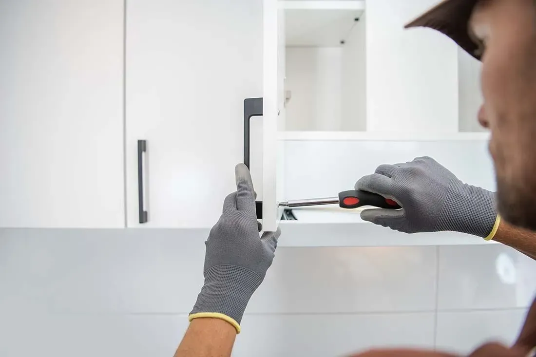 A gloved installer attaching a black bar handle to a new white cabinet door