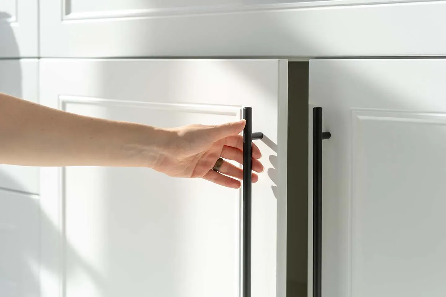 A hand opening a new white cabinet door with a slim black bar pull