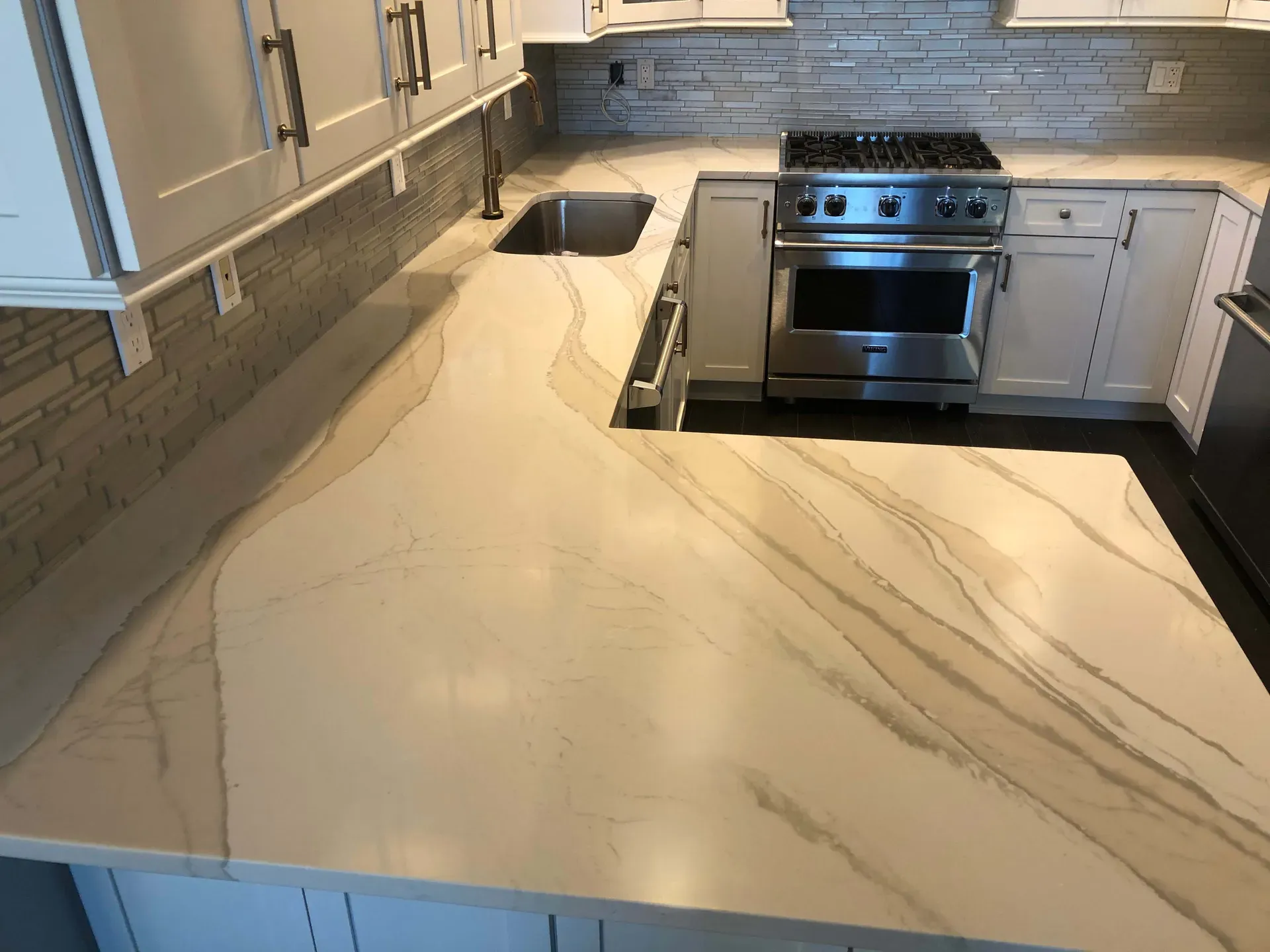 A white quartz countertop with soft grey veining running the length of a refaced kitchen, past an undermount sink to a range