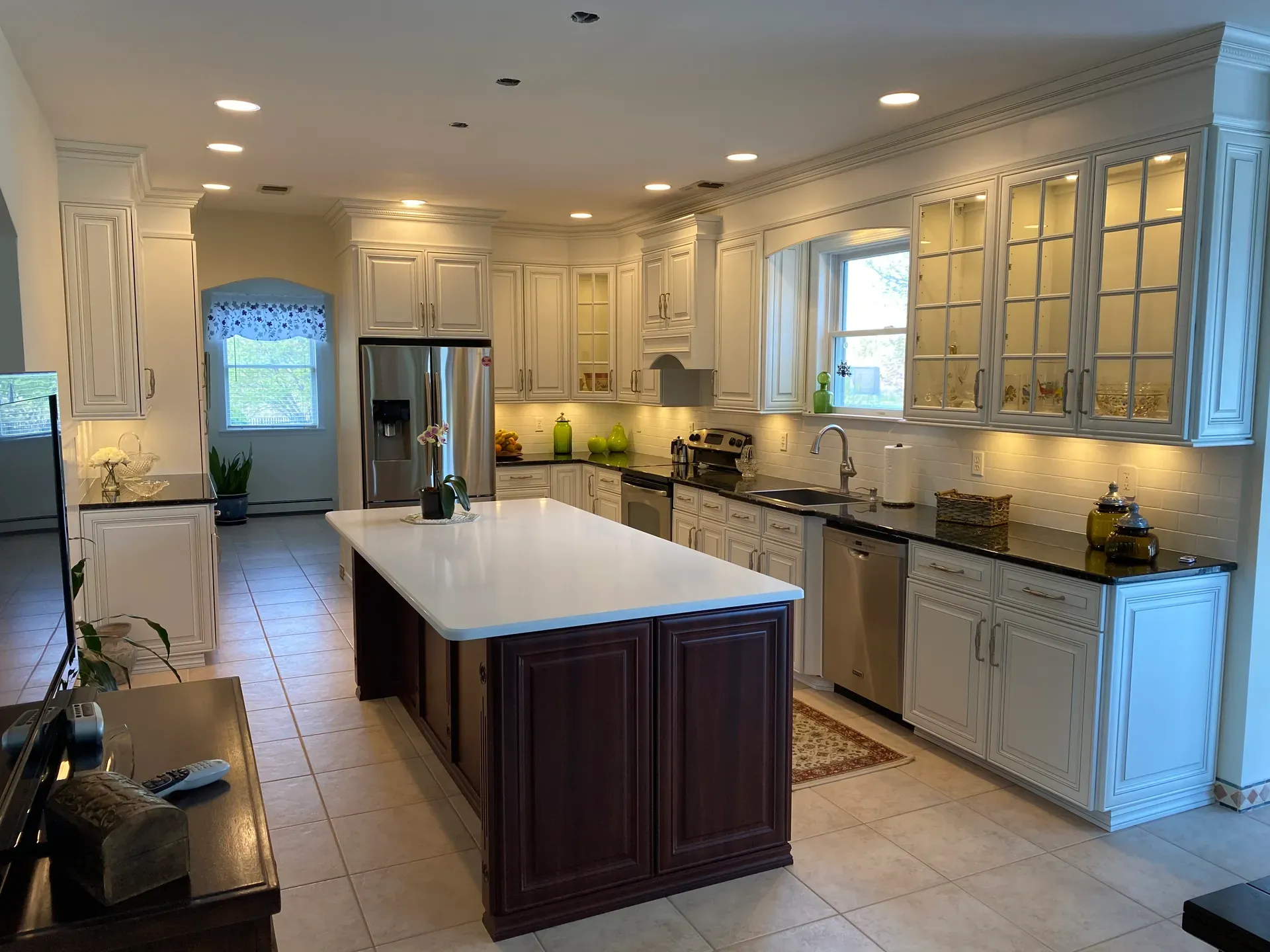 A completed kitchen with cream raised-panel cabinets, glass-front upper doors, dark granite counters and a mahogany island under a white quartz top