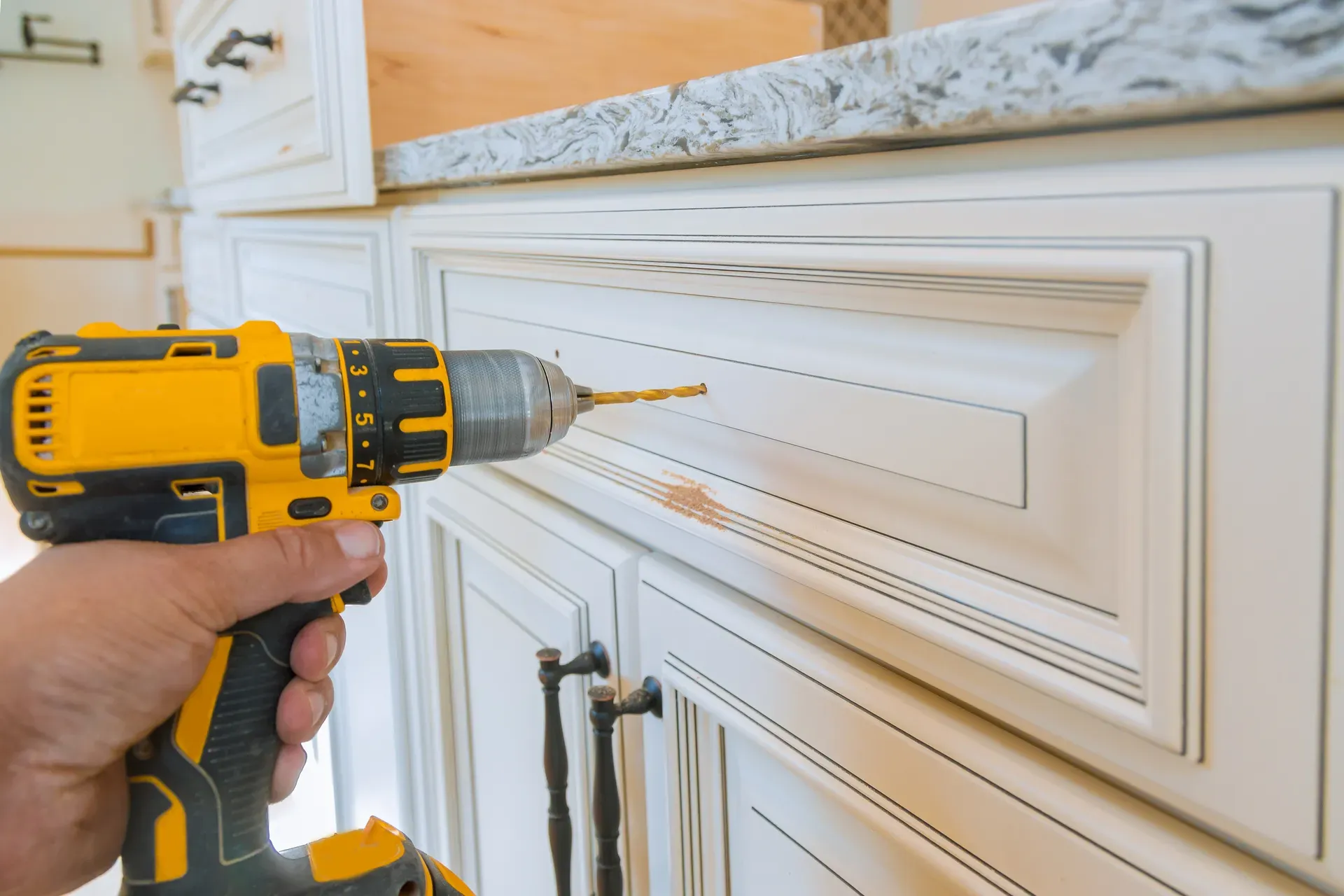 A cordless drill boring the handle holes in a refaced white cabinet door