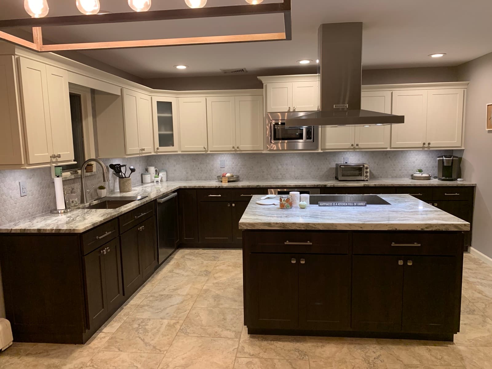 A wide island topped with heavily veined marble-look stone, between espresso shaker base cabinets and cream shaker uppers