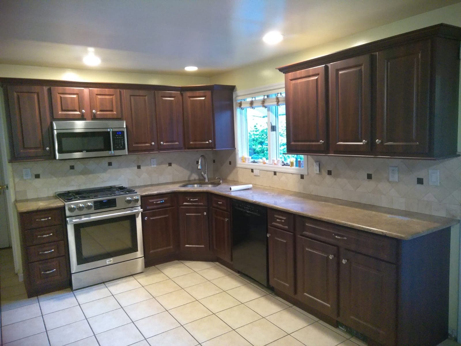Dark cherry raised-panel cabinets running two walls of a kitchen, with a carved border on every door and brushed-nickel handles