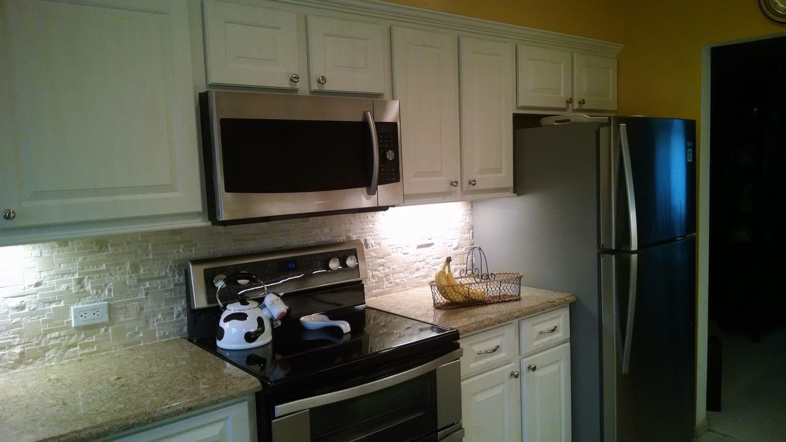 Cream raised-panel cabinets around a stainless over-range microwave, with a split-face stone backsplash and granite counters