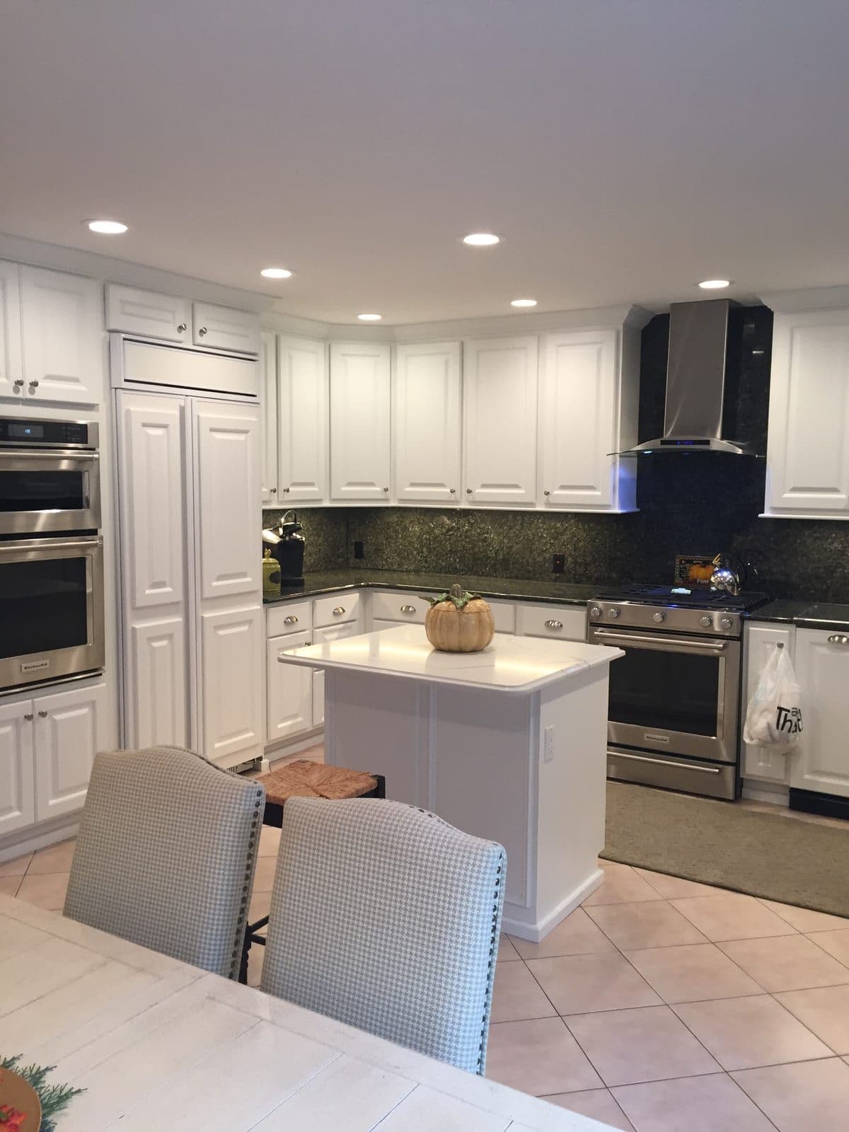 A white raised-panel kitchen with a small central island, dark green granite counters and stainless wall ovens