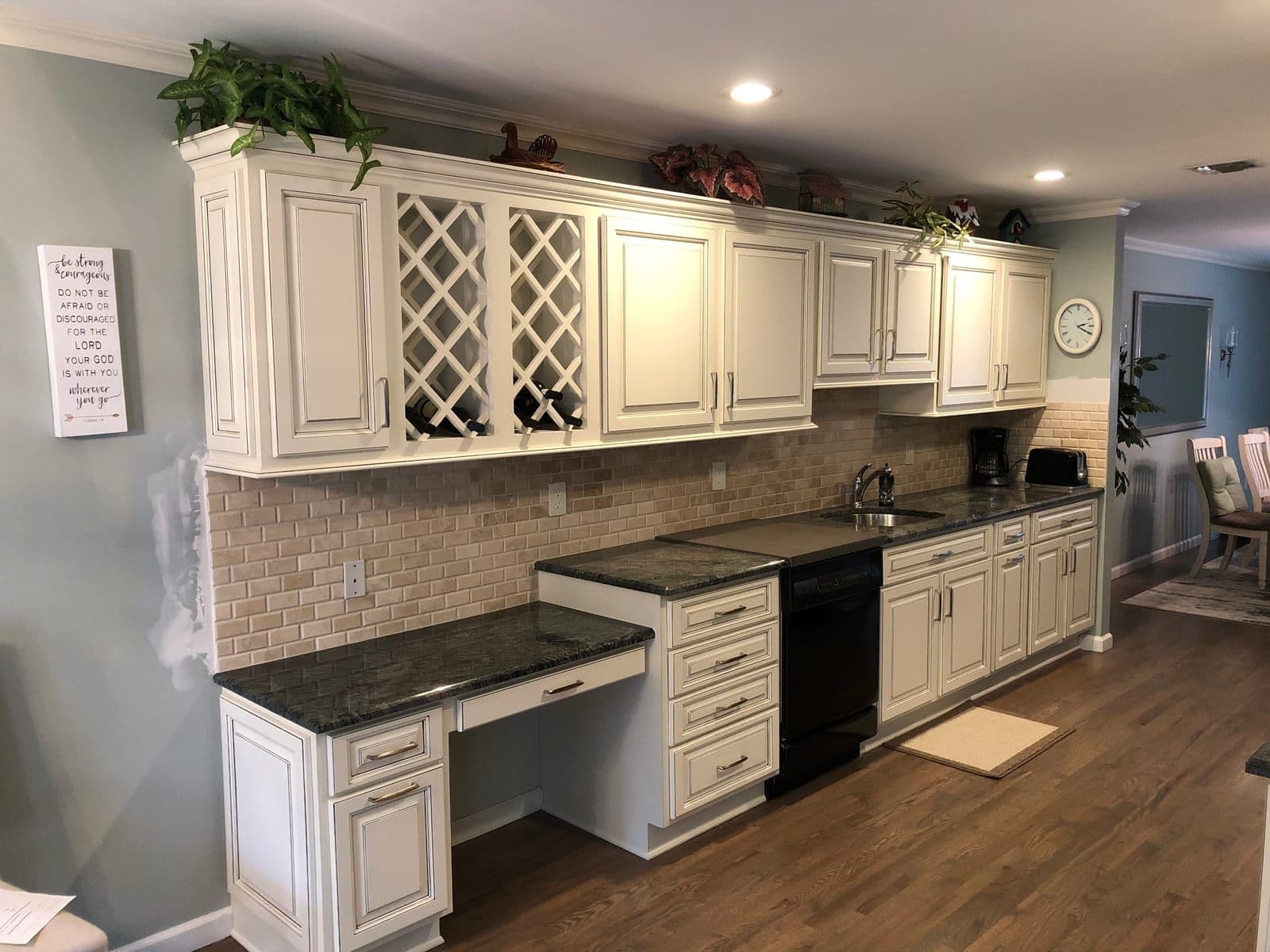 Cream glazed raised-panel cabinets with a built-in wine lattice and desk return, over green granite and a tumbled-brick backsplash