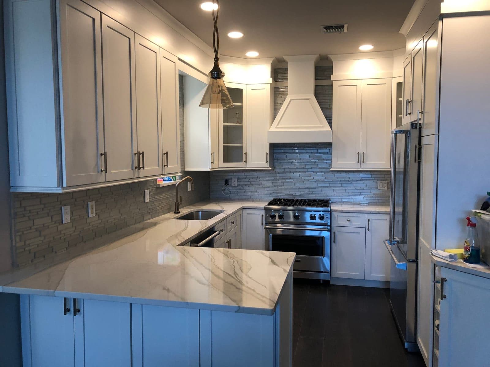 A white shaker kitchen with a custom paneled hood, marble-veined counters and a pale glass mosaic backsplash