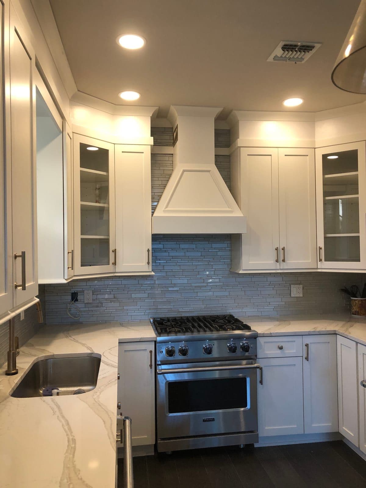 A professional stainless range beneath a custom white hood, framed by glass-front shaker uppers and marble-veined counters