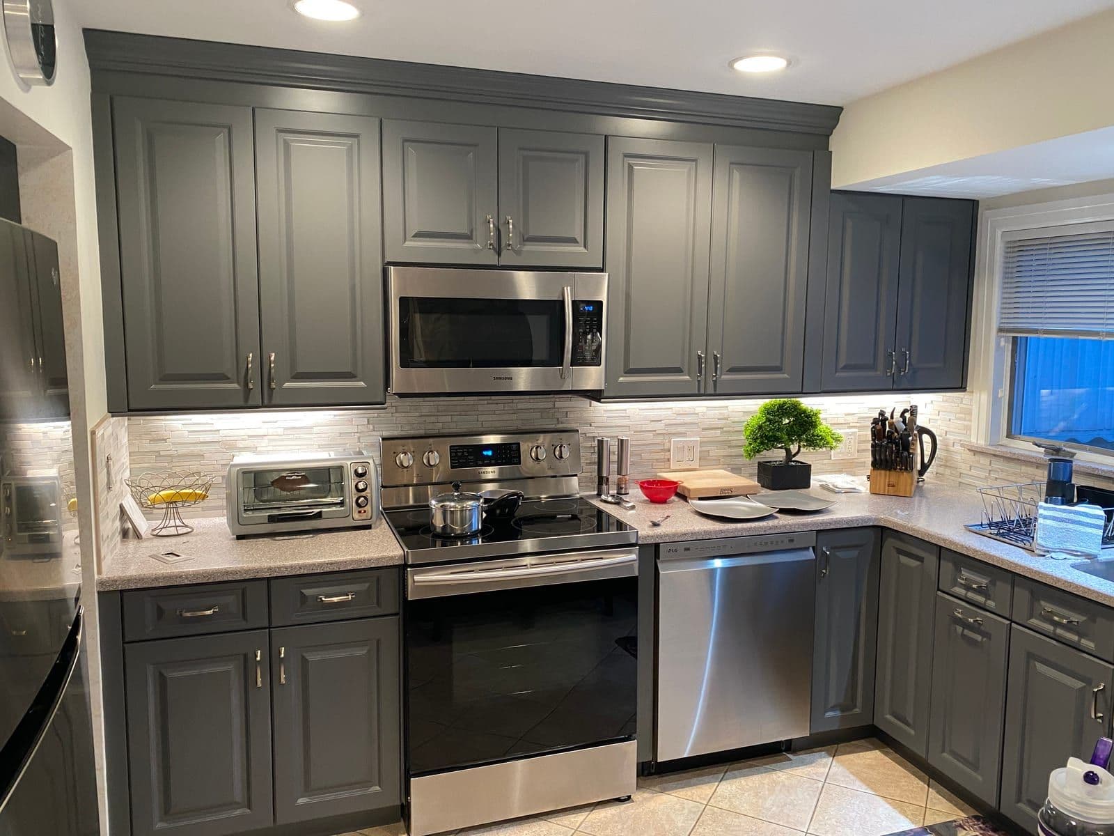 Charcoal-grey raised-panel cabinets with stainless appliances, a stone mosaic backsplash and speckled counters