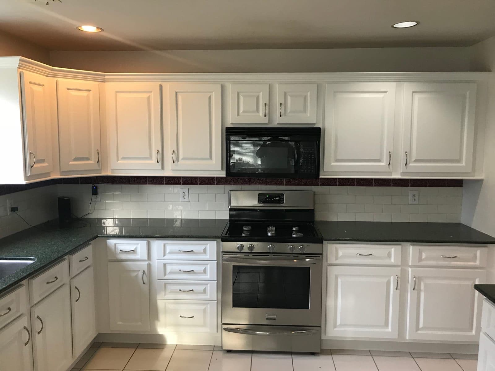 White raised-panel cabinets over dark green granite, with a white subway backsplash and a stainless gas range