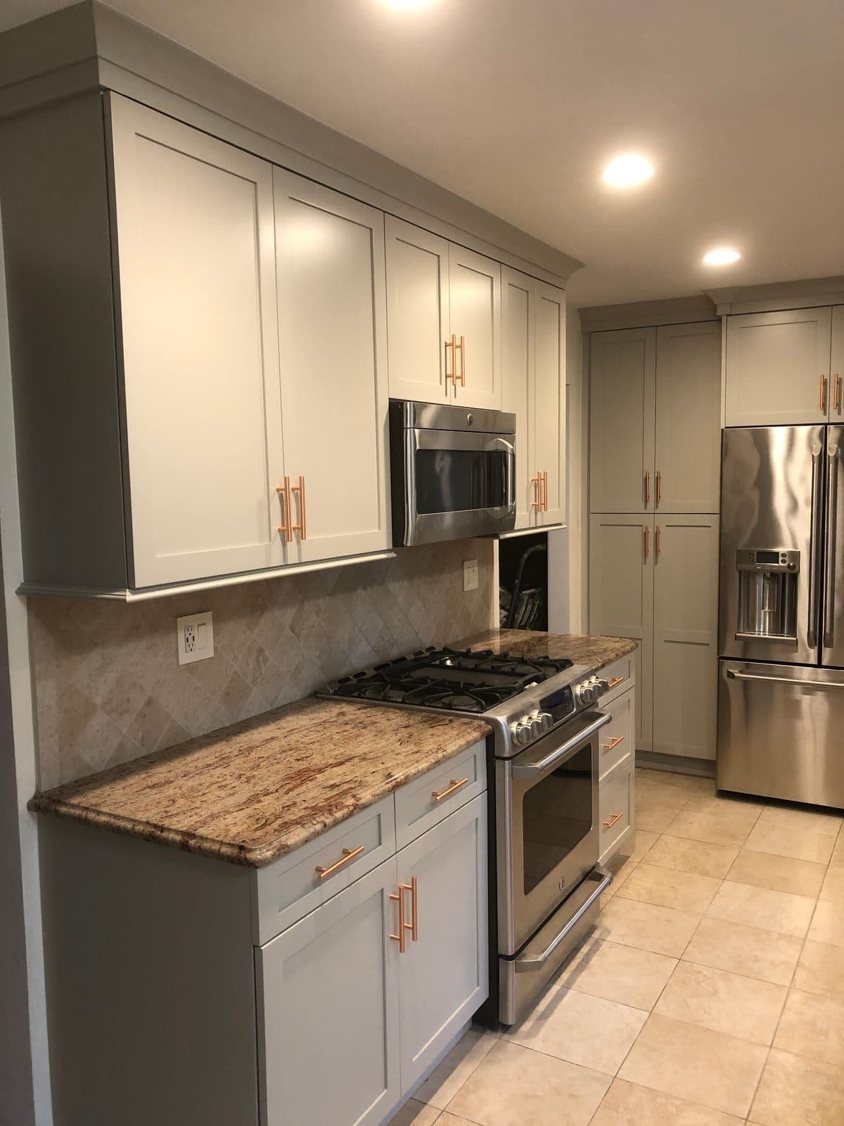 Pale grey shaker cabinets with brushed copper bar pulls, beside a stainless range and a warm-toned granite counter