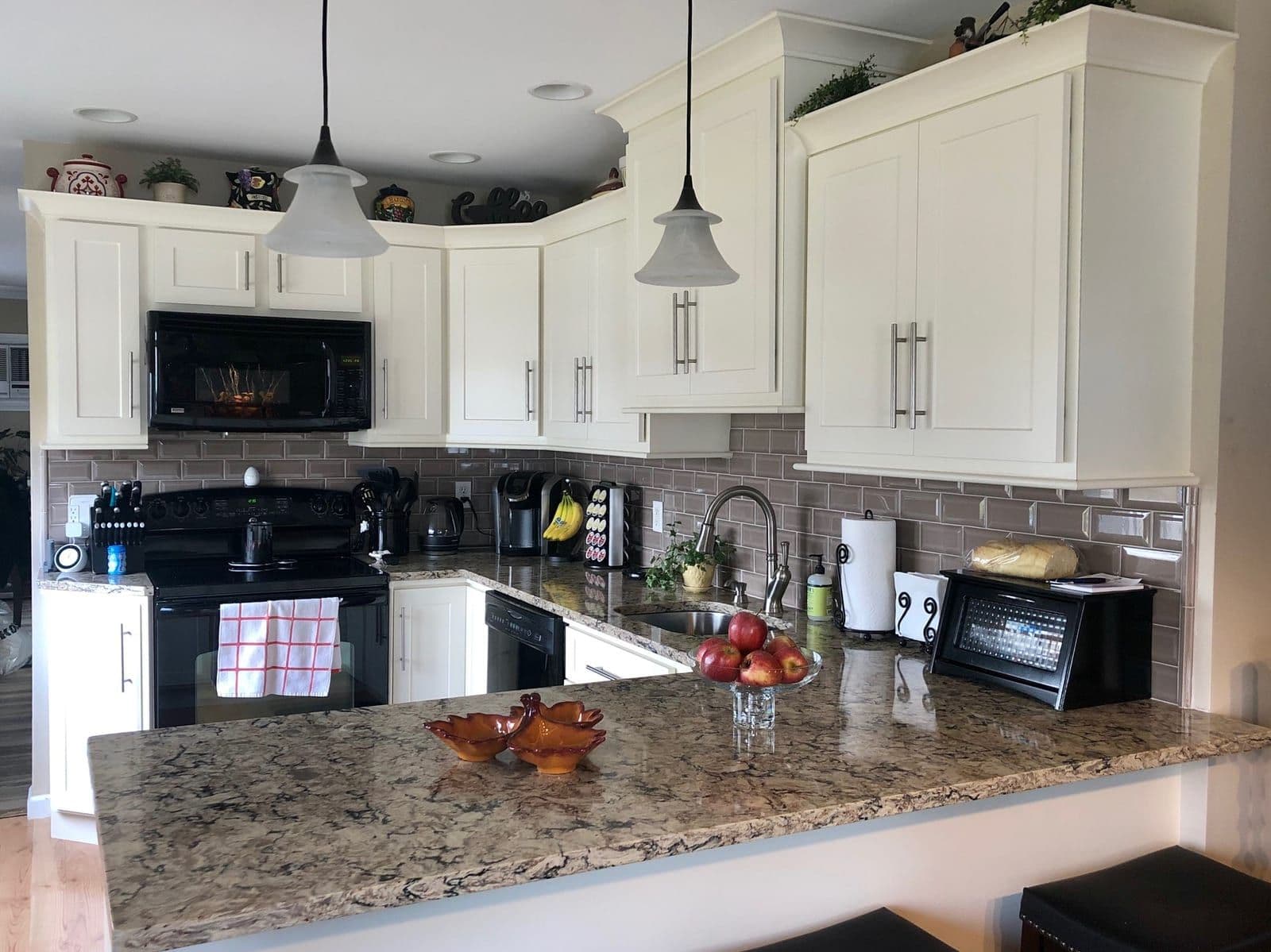Cream shaker cabinets around a granite peninsula, with a taupe glass subway backsplash and brushed-steel bar pulls