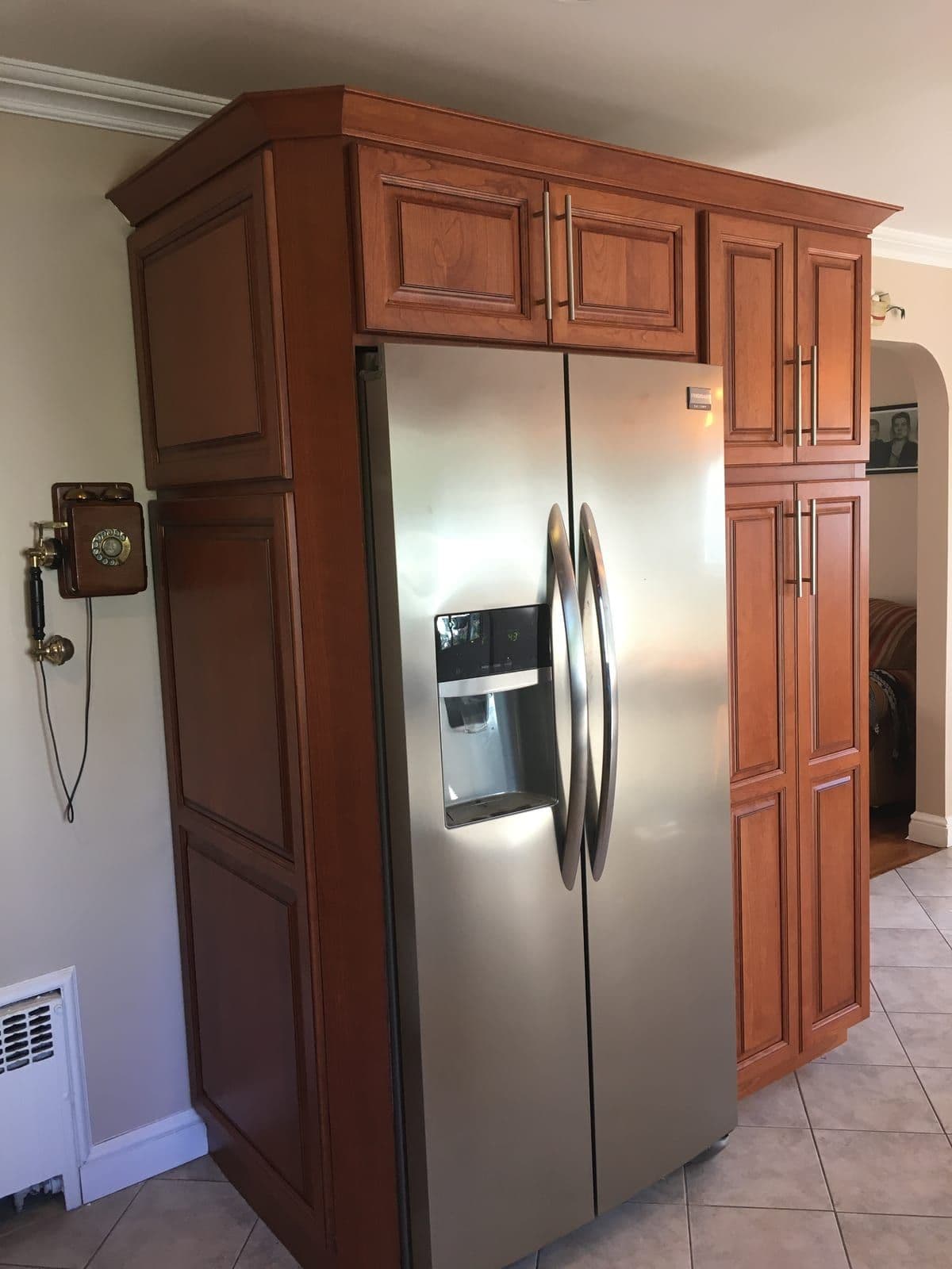 A tall run of cherry raised-panel cabinets built around a stainless side-by-side refrigerator, with a matching crown and brushed-steel bar pulls
