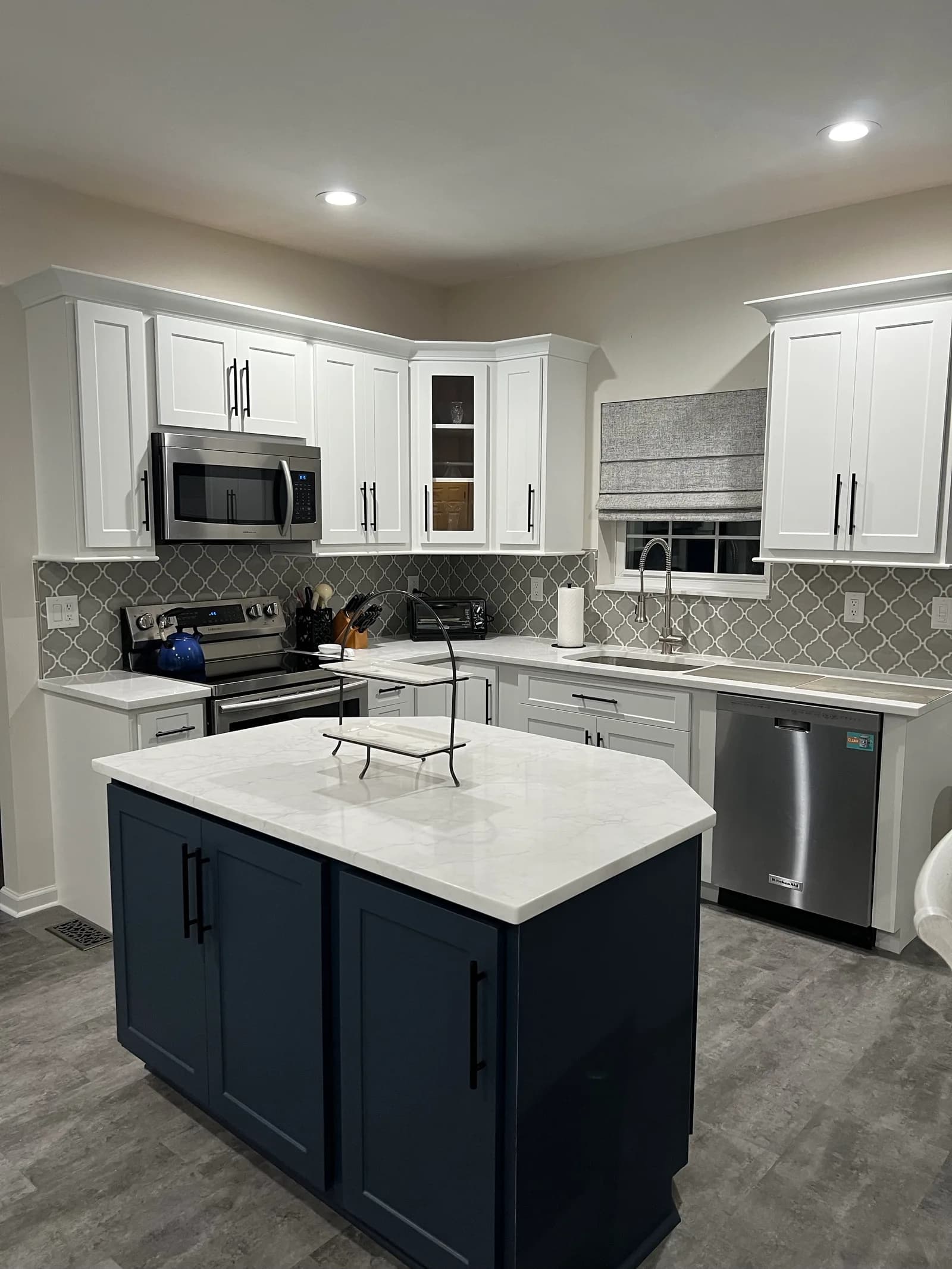 A white shaker kitchen with a navy island, marble-look quartz top and a grey arabesque-tile backsplash