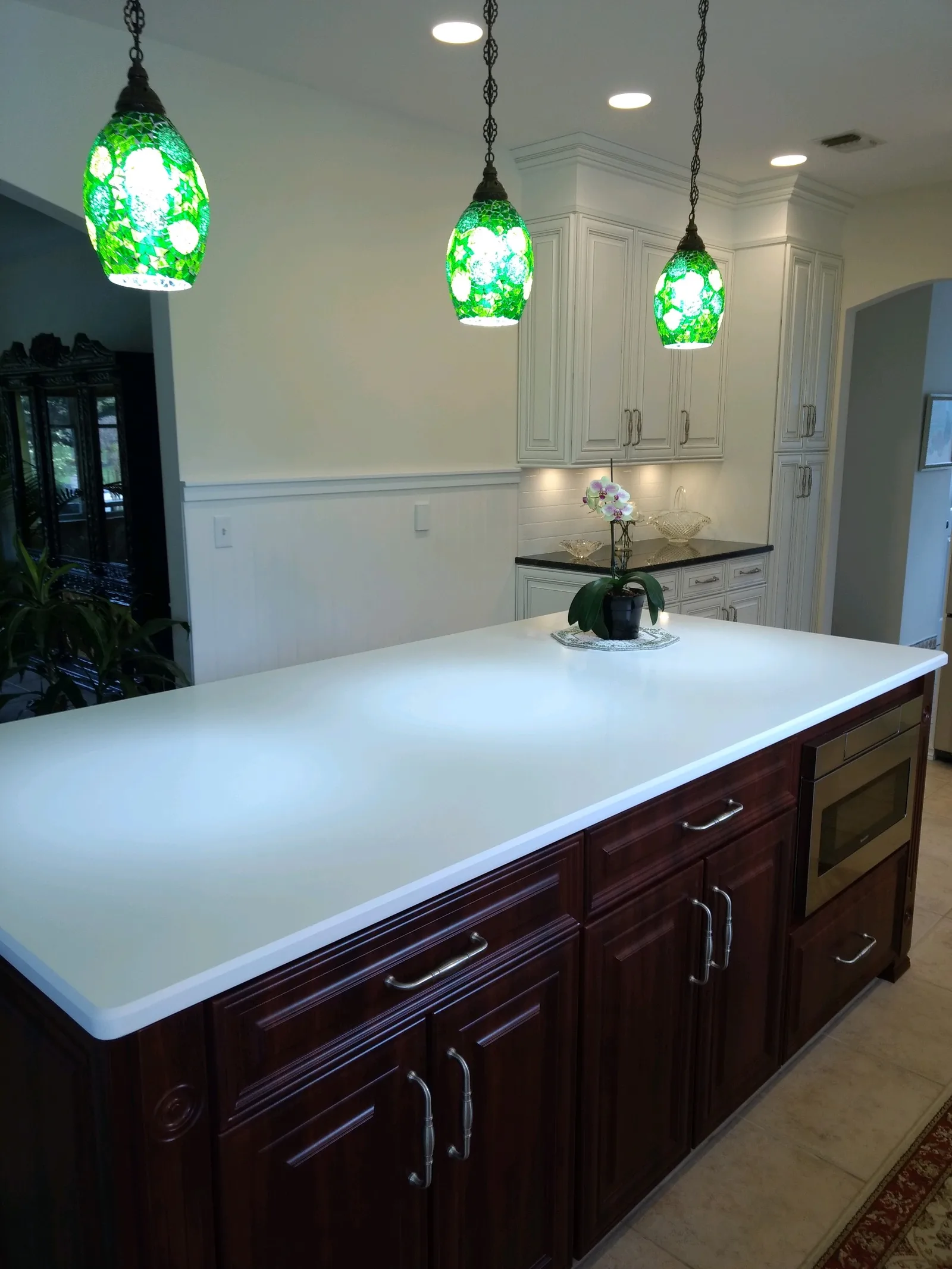 A dark cherry island with a built-in stainless microwave under a white quartz top, beside cream glazed perimeter cabinets