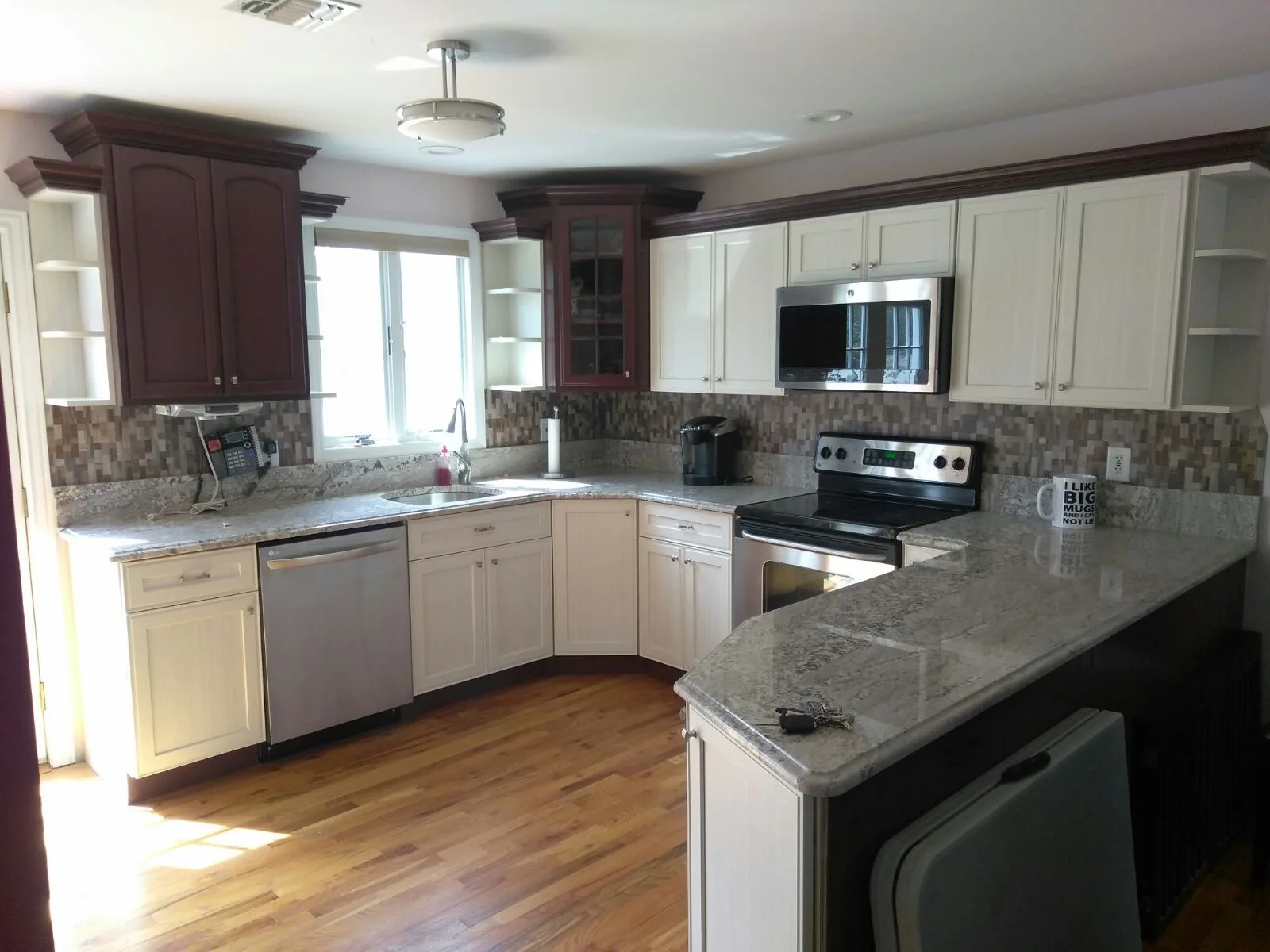 A refaced kitchen pairing antique-white beadboard-style doors with dark burgundy uppers over a grey granite peninsula
