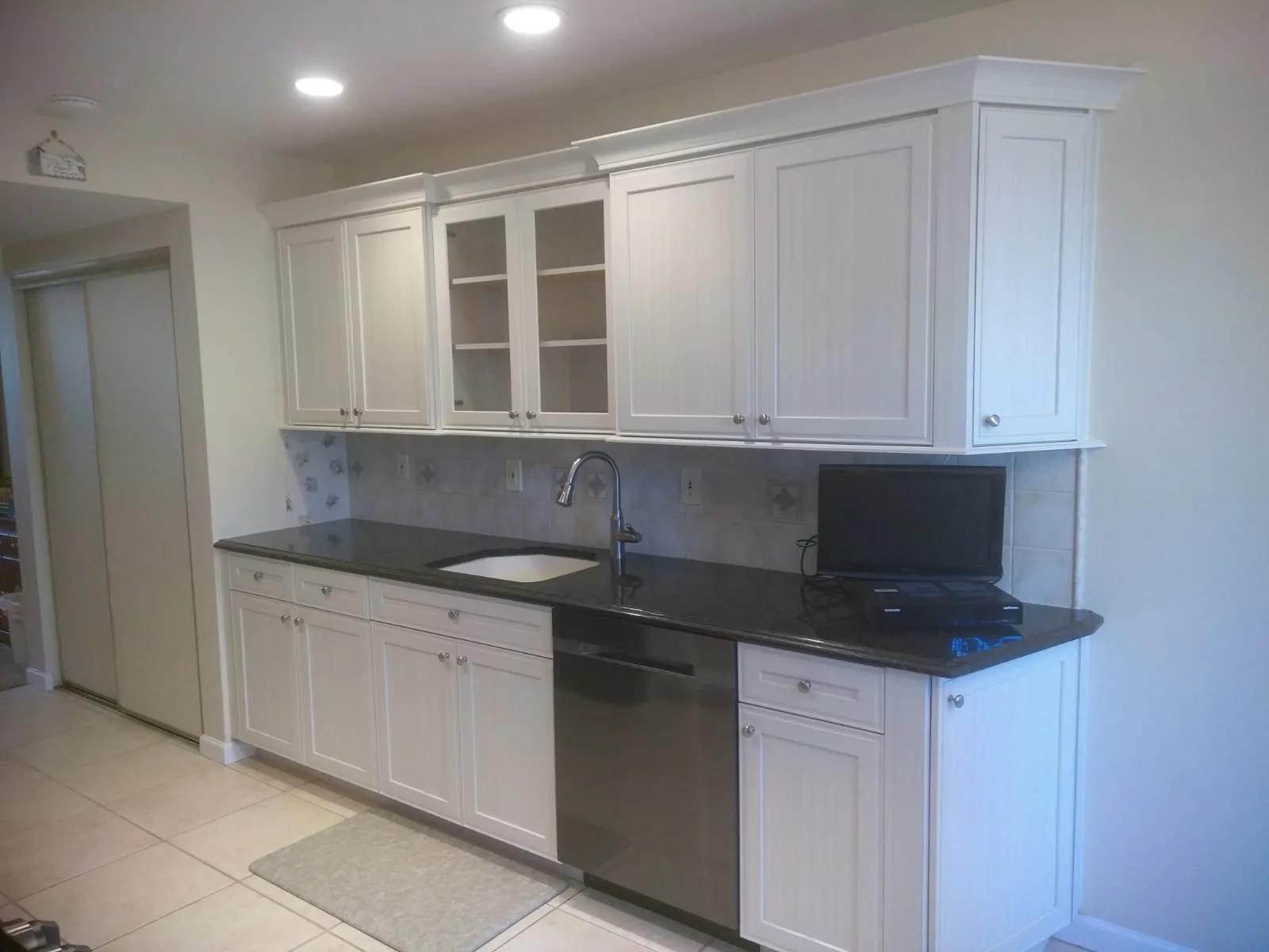 A white galley run with glass display uppers, black granite counters and a black stainless dishwasher