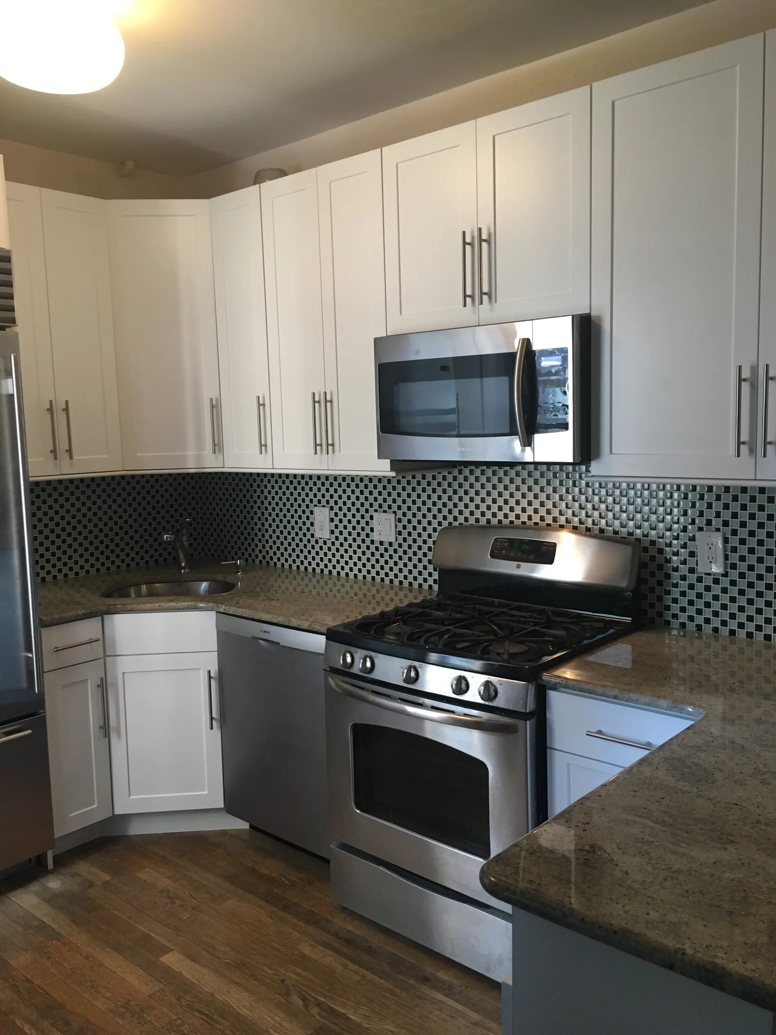 White shaker cabinets to the ceiling with long brushed-steel pulls, a stainless range and microwave, a black-and-white mosaic backsplash and granite counters