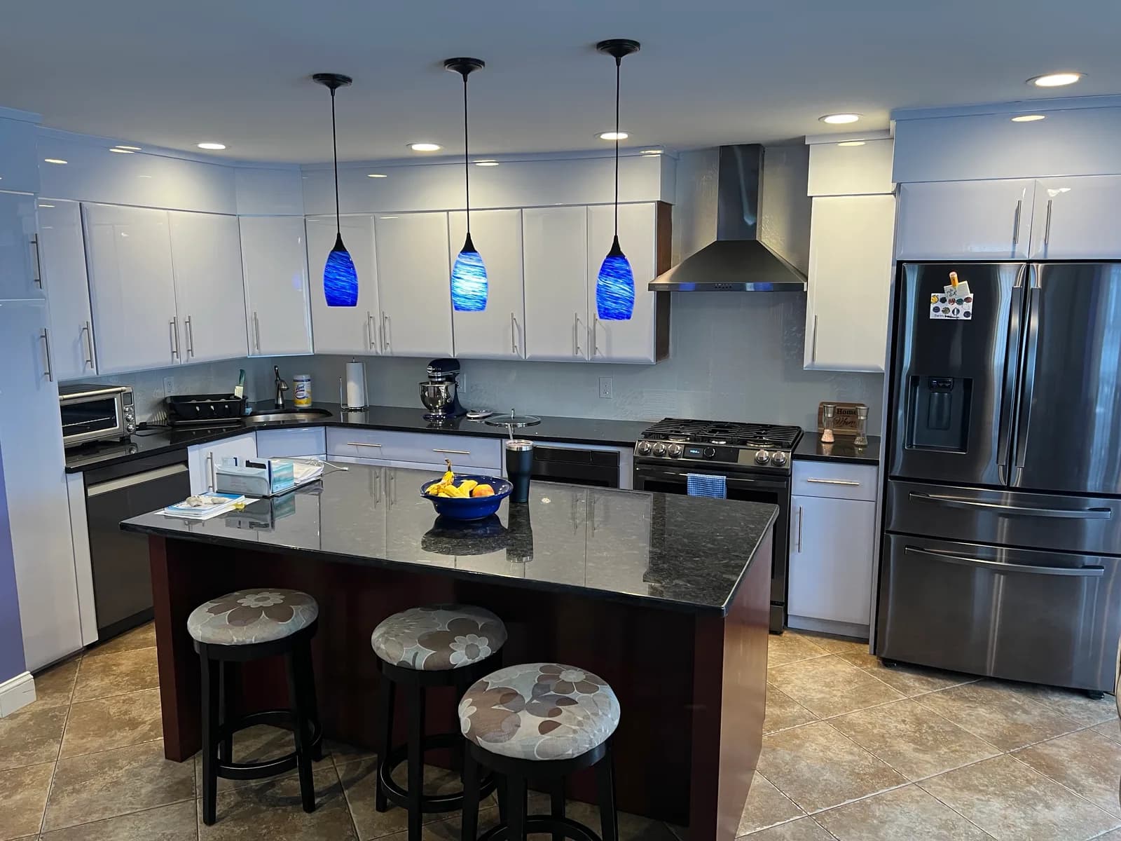 A kitchen with glossy white flat-panel cabinets, black granite counters and a dark wood island lit by three blue art-glass pendants