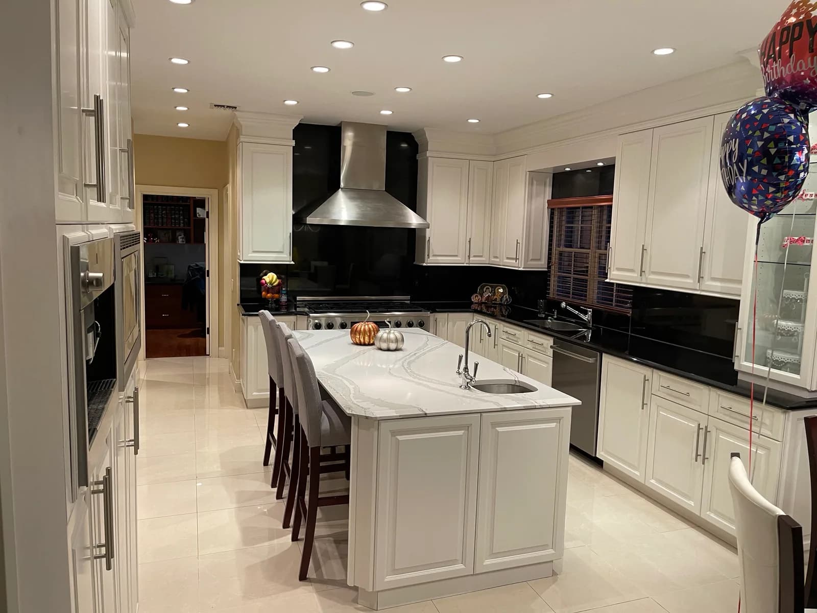 A white kitchen with a black tile backsplash, stainless range hood, and a large island with a gray waterfall-edge stone countertop