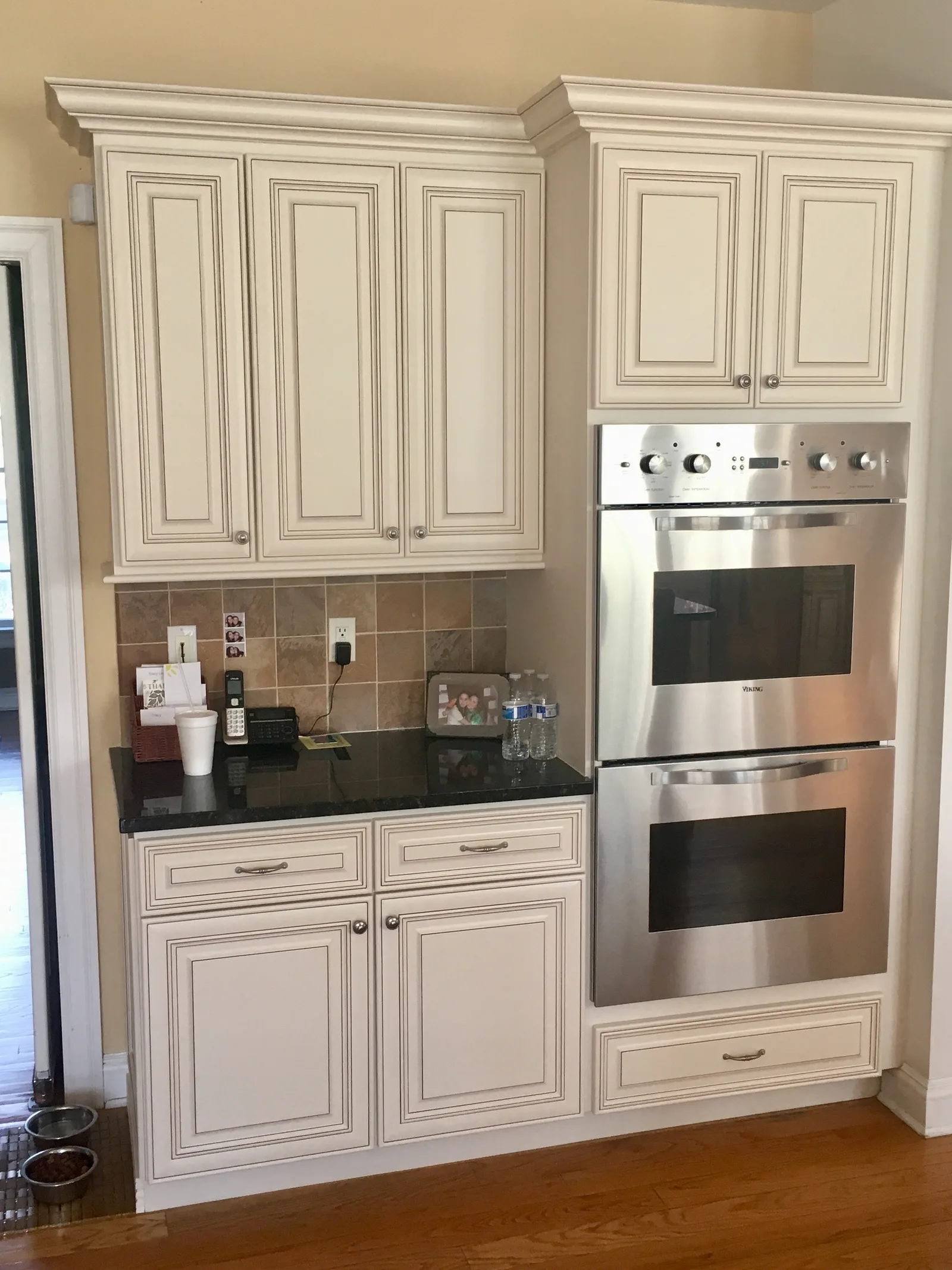 Cream raised-panel cabinets with a black granite countertop and a stainless double wall oven set into the cabinet run