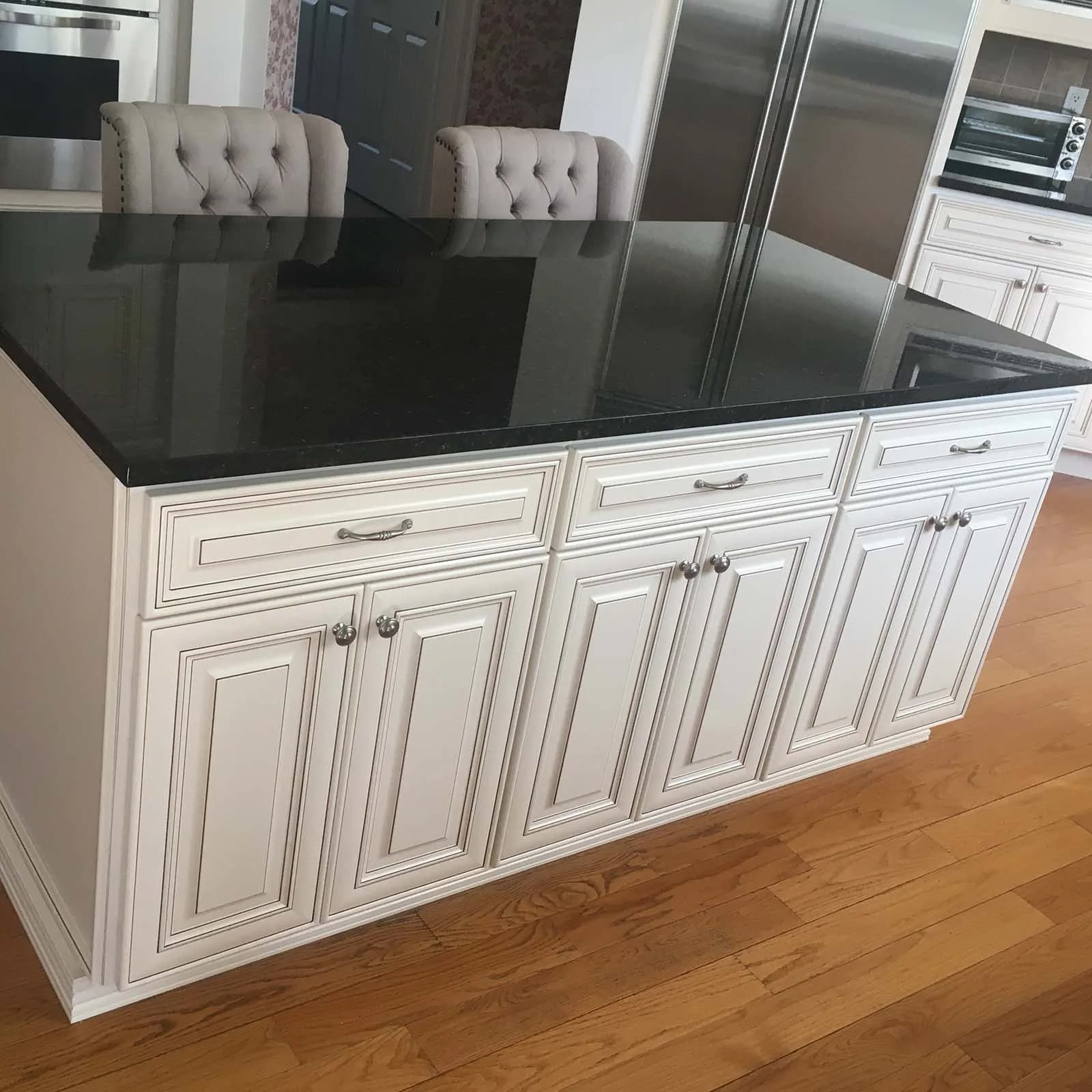 The island in the same cream raised-panel kitchen, with a black granite top, brushed-nickel pulls and tufted barrel-back stools