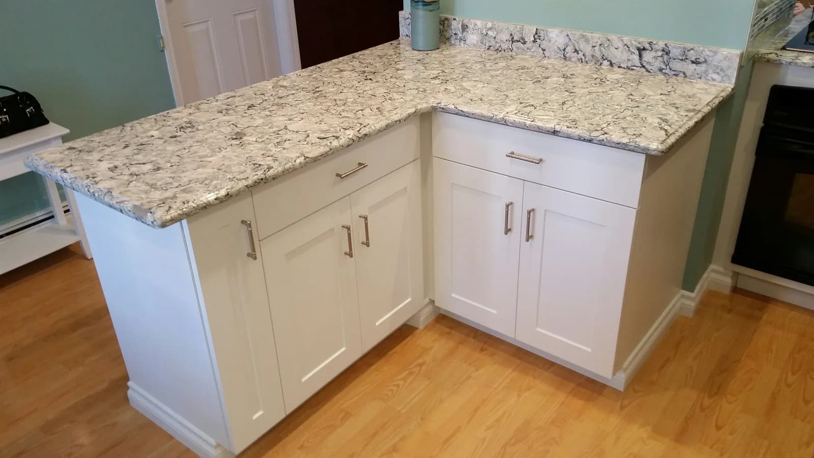An L-shaped white shaker peninsula with a grey-veined quartz top and matching backsplash ledge
