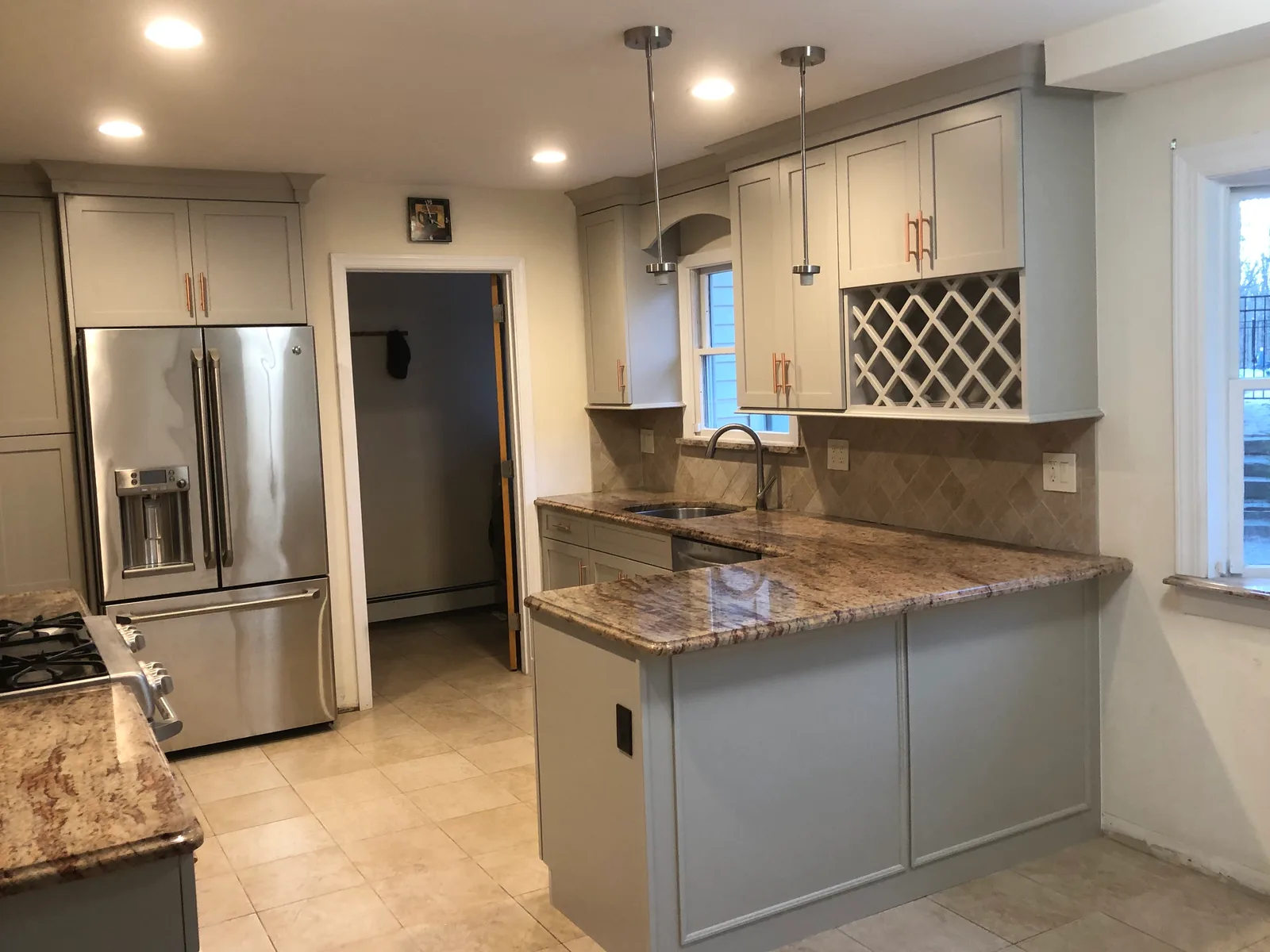 Grey shaker cabinets with rose-gold pulls, a built-in wine lattice and granite counters over a tumbled-stone backsplash