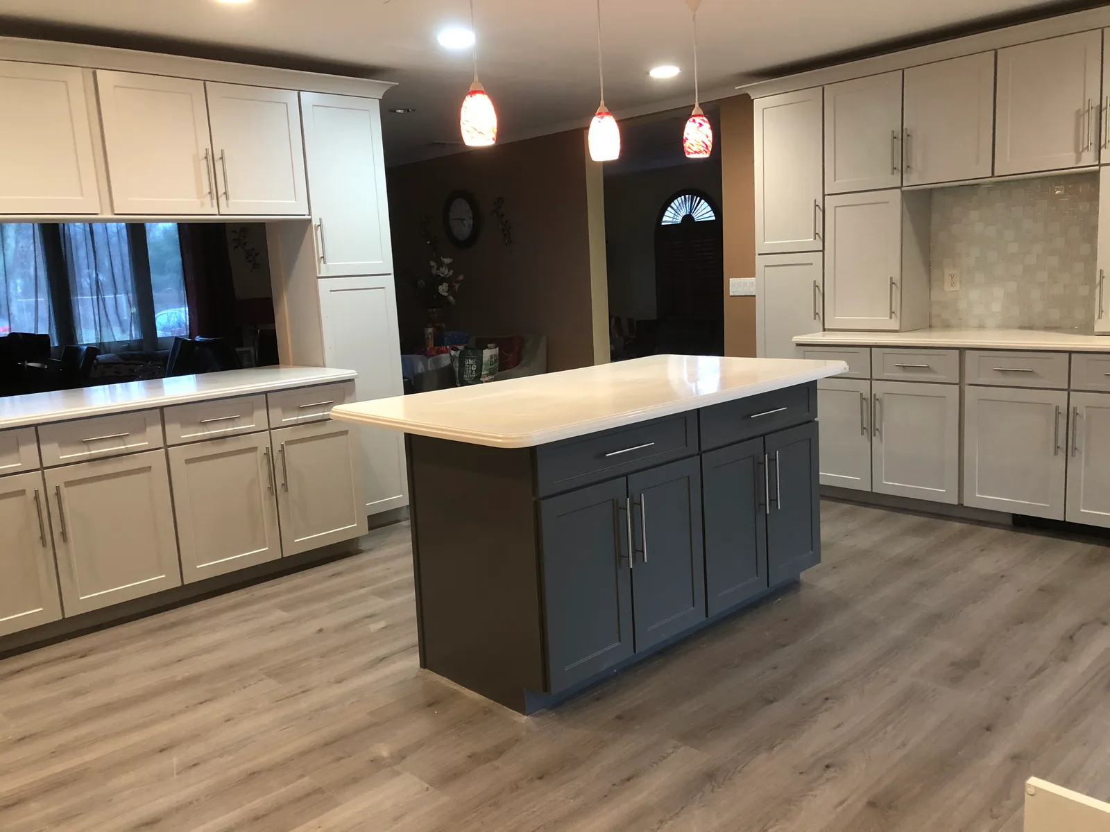 A pale grey kitchen with a charcoal shaker island, white quartz tops and wood-look plank flooring