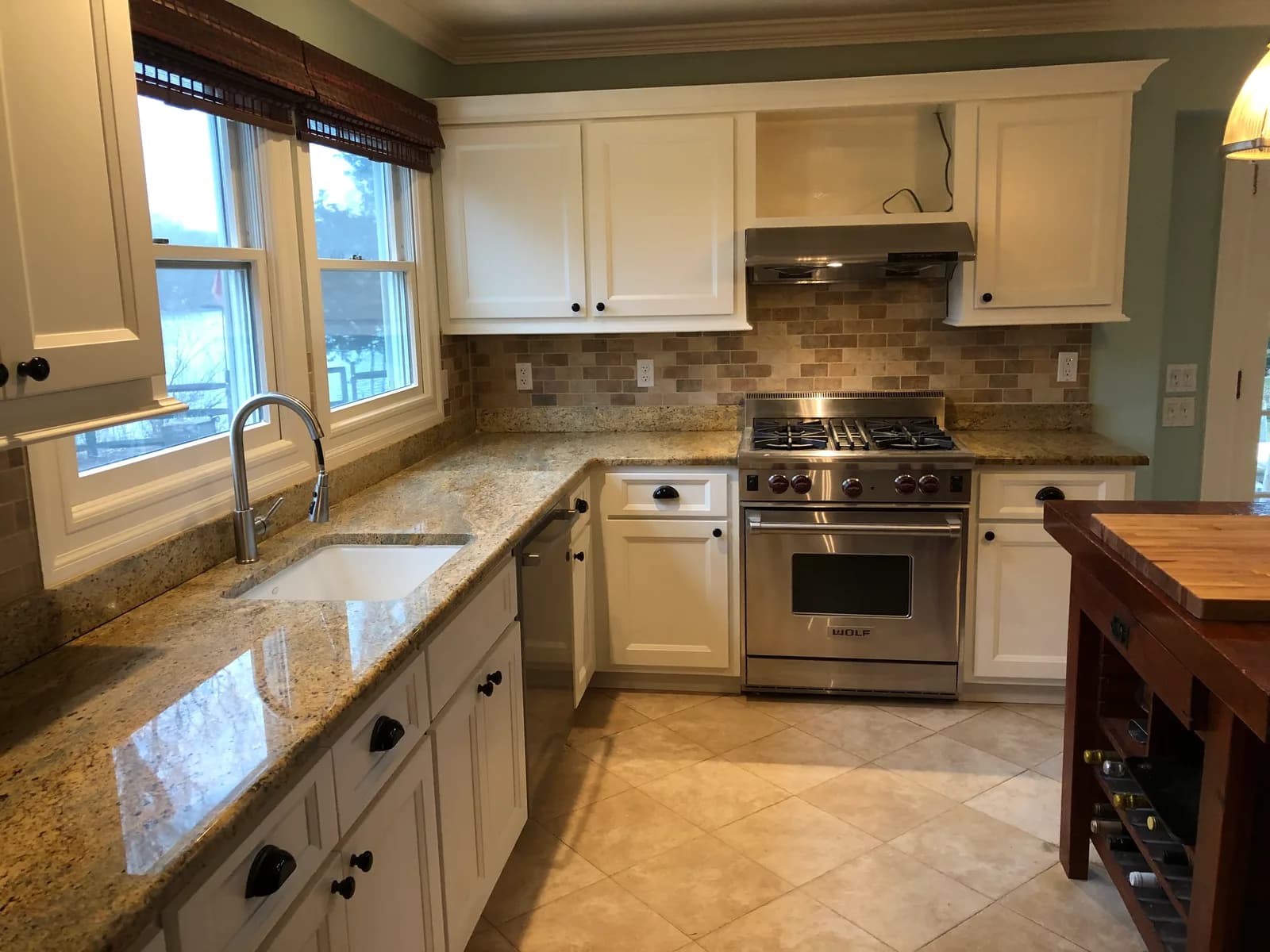 White cabinets with dark cup pulls around a stainless range, under golden granite and a brick-pattern stone backsplash