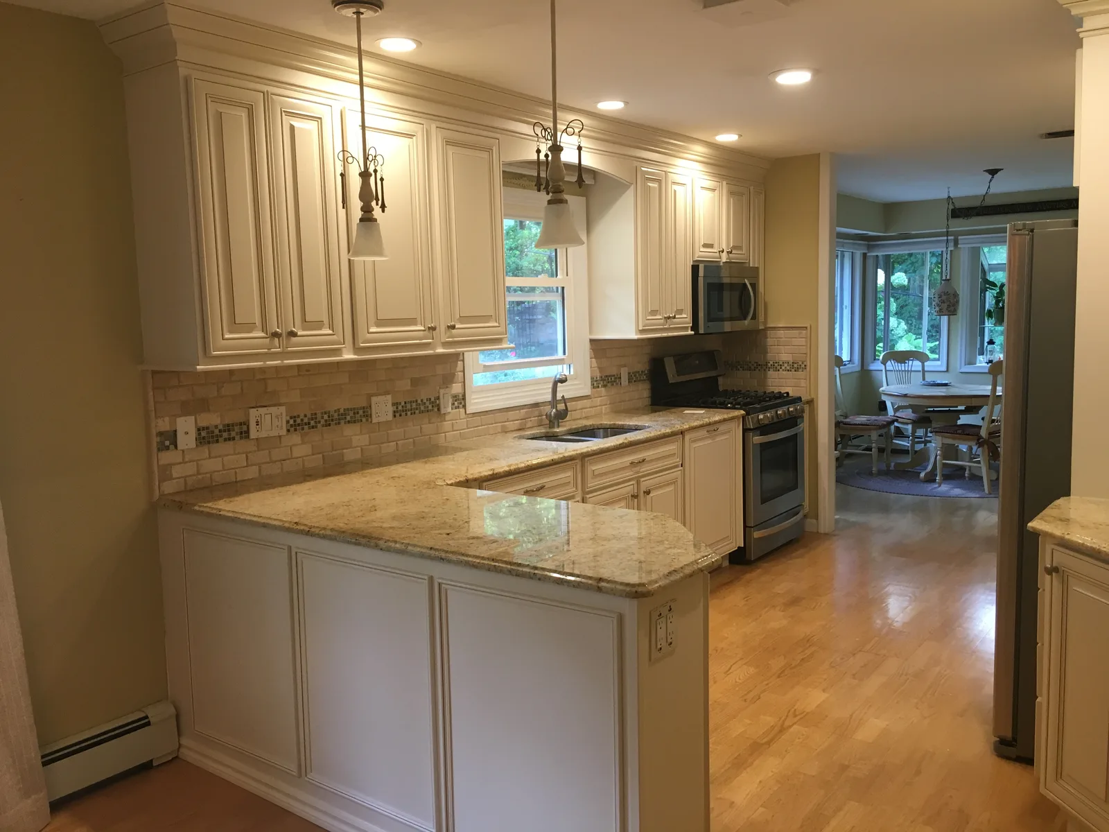 Cream glazed cabinets with scrolled pendant lights, a travertine subway backsplash and golden granite counters
