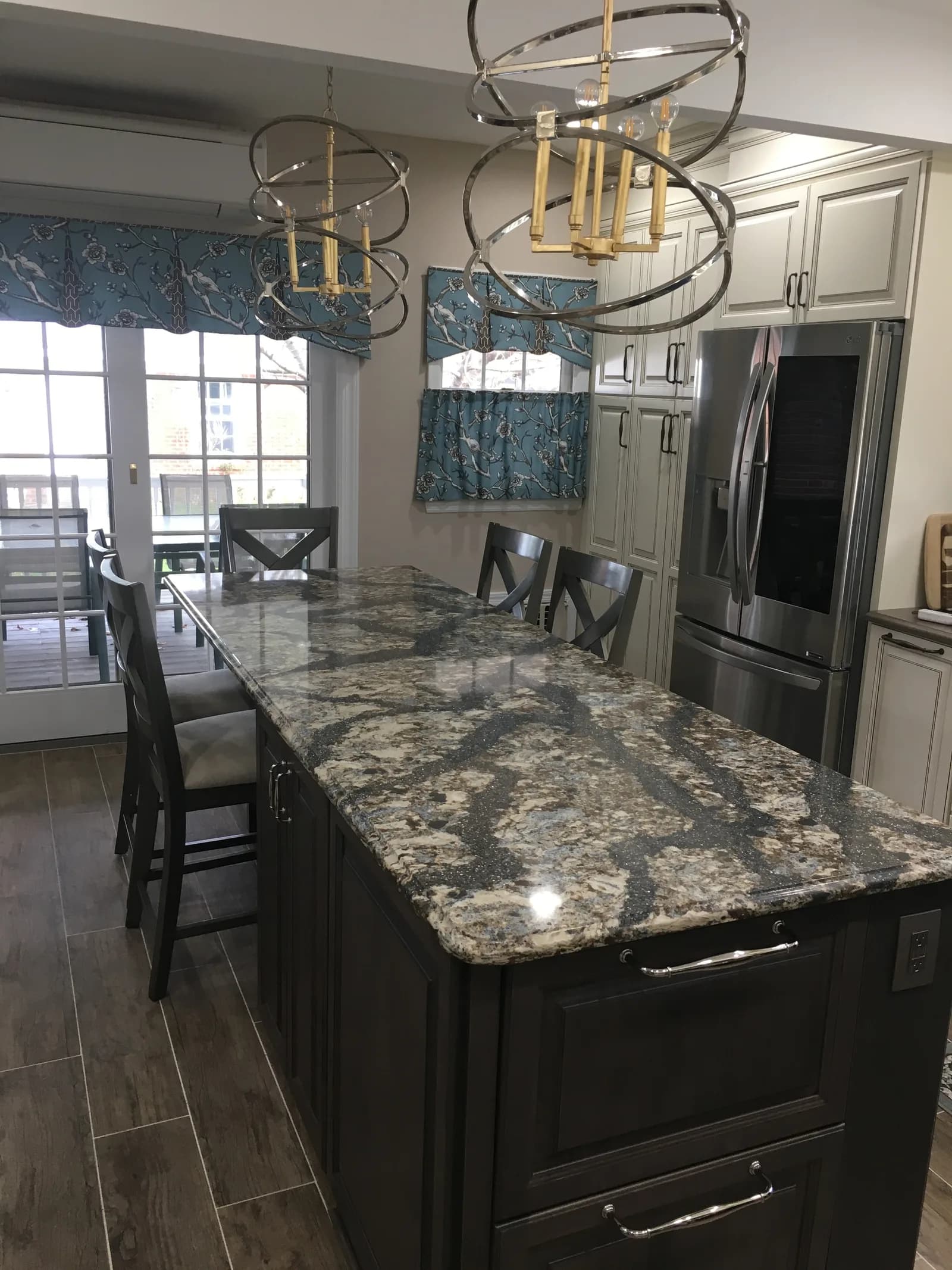 A charcoal island under dramatic blue-grey granite, with cream panelled cabinets and chrome orb chandeliers behind