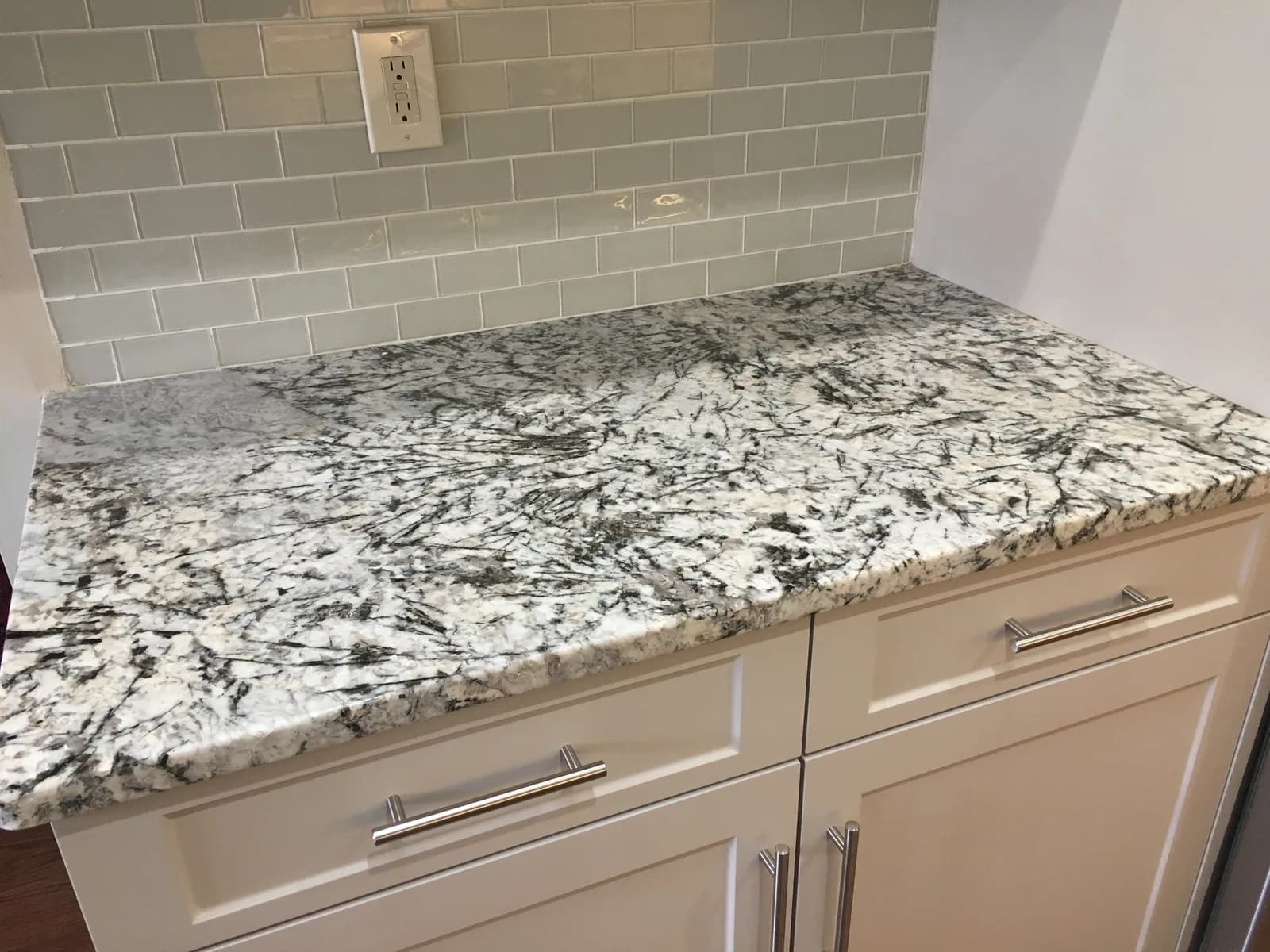 Close-up of a speckled granite countertop against a pale green glass subway-tile backsplash
