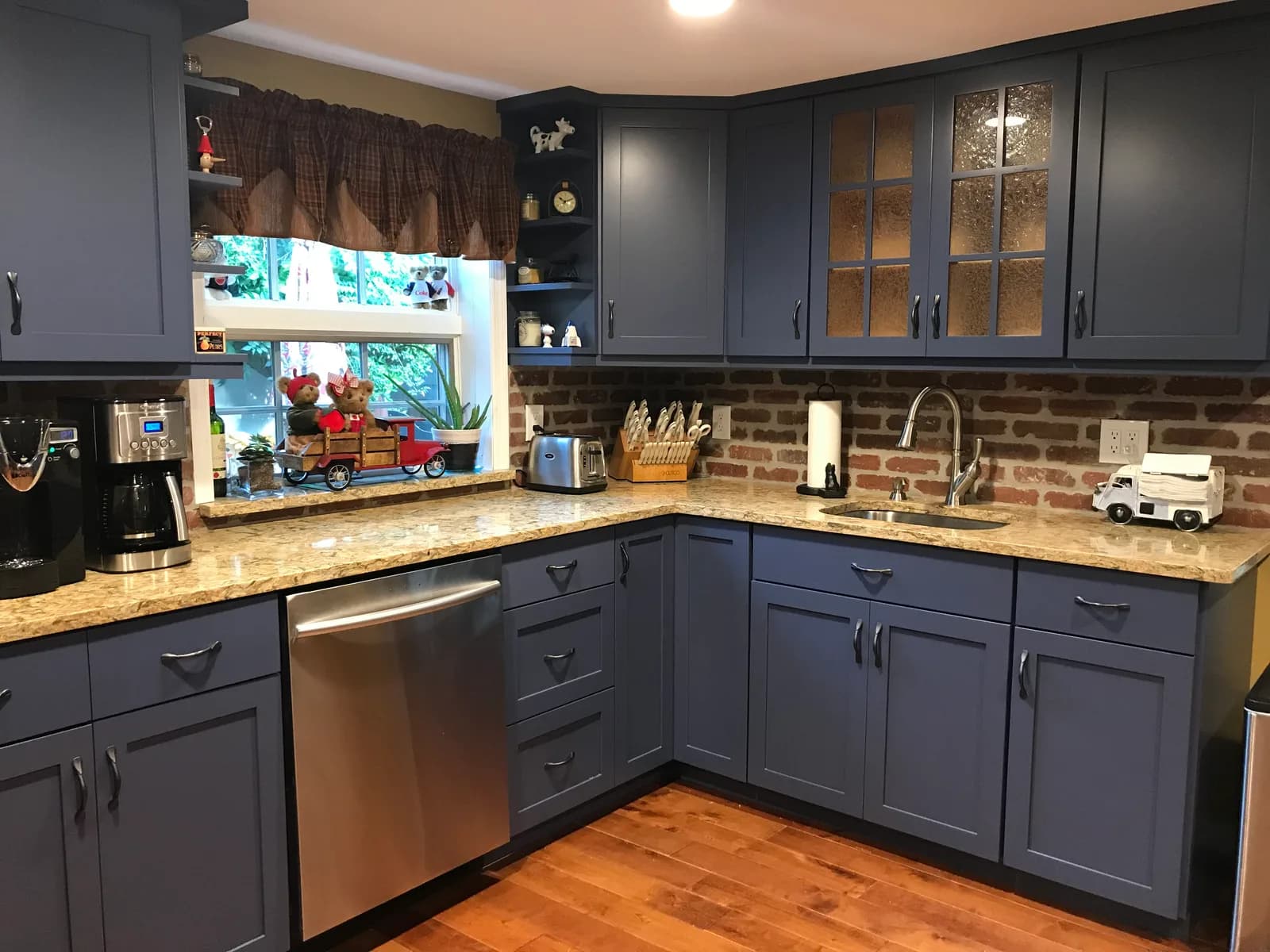 A slate-blue shaker kitchen with glass-front uppers, cream granite counters and an exposed-brick backsplash